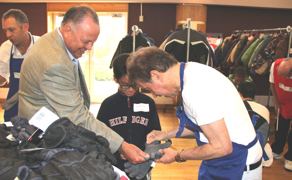James R. Gonzalez, President and CEO of University Hospital (l), and a NCJW/Essex volunteer (r) help a youngster select winter gloves at the Back 2 School Store.