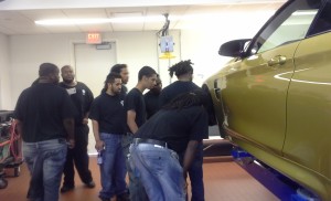 NCC automotive trainees inspected a vehicle undergoing repair at the BMW shop. In addition to BMW, NCC partners with other automakers, such as Ford, and local employers, to place trainees in internships as part of the Automotive Technician Employment and Training Program.