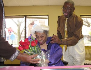 Food Service Director Jackie Henry, left, hands red long-stemmed roses to Edna Van Dunk, who celebrated her 100th birthday at New Community Extended Care Facility.
